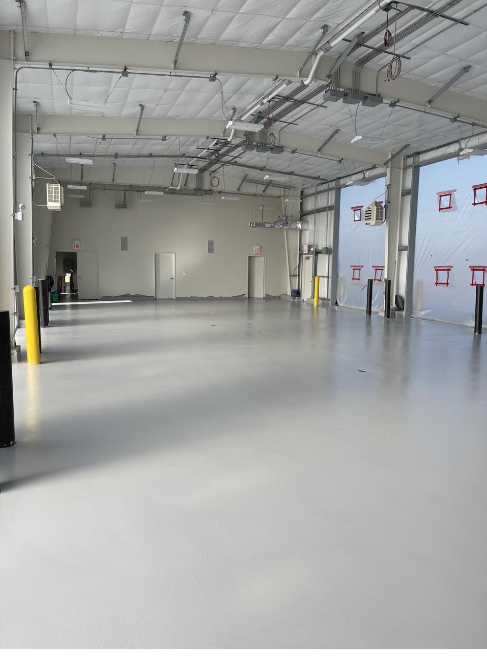 Finished light gray epoxy floor in a large open industrial bay with safety bollards